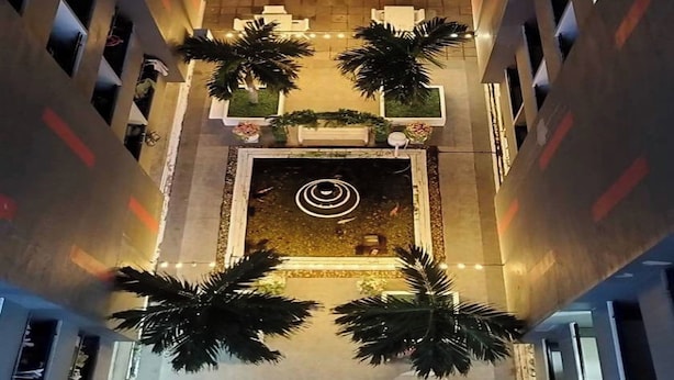 Een hoog gebouw met een centrale binnenplaats, terrasjes, palmbomen en een decoratieve waterpartij.