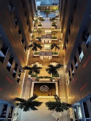 Un edificio de gran altura con un patio central que ofrece mesas al aire libre, palmeras y una fuente decorativa.