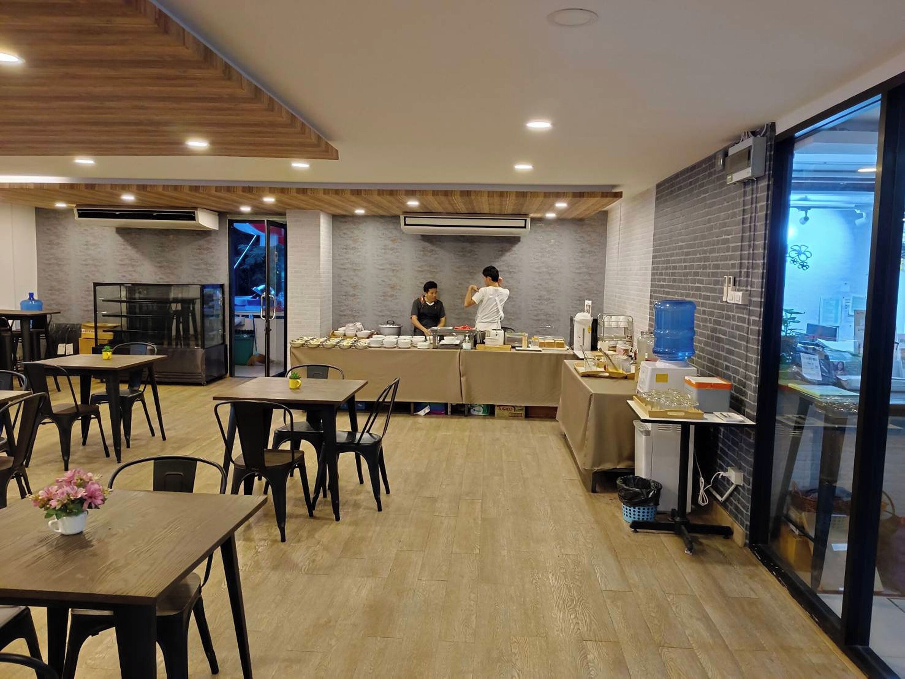 Un café moderno con suelo de madera, mesas, sillas y una barra donde un empleado prepara comida.