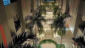 Een binnenplaats met een centrale fontein, omgeven door palmbomen en lichtjes, met zitplekken en een uitzicht op een gebouw op de achtergrond.