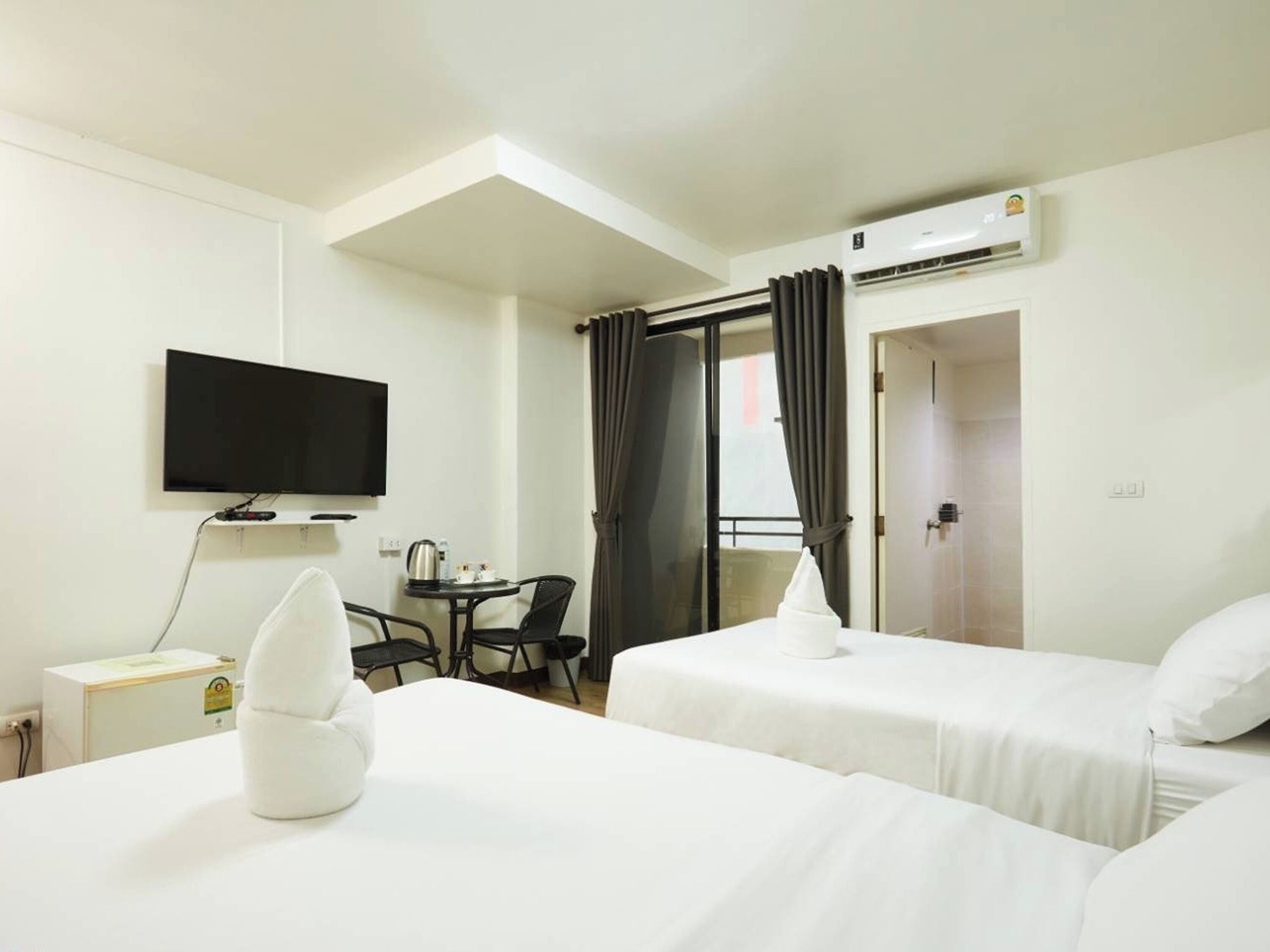 A hotel room with two beds, a TV, a desk with a chair, and an air conditioning unit.