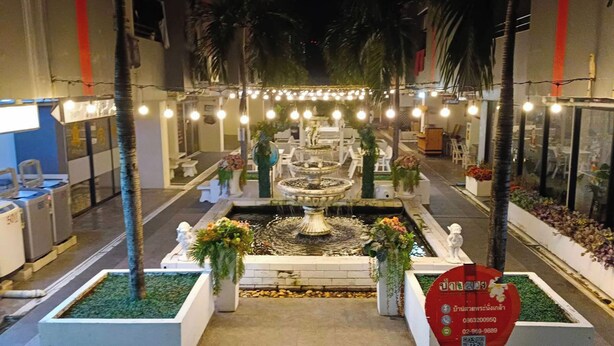 Un patio interior bien iluminado con una fuente central, rodeado de zonas de estar y plantas en macetas.