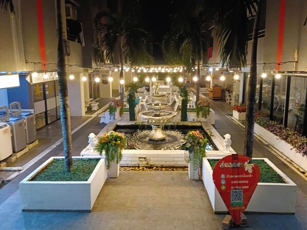 Un patio interior bien iluminado con una fuente central, rodeado de zonas de estar y plantas en macetas.
