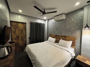 A modern hotel room with a large bed, a ceiling fan, an air conditioning unit, a wooden door, and a small table with a kettle. - Aariv Comforts Baga (Baga)
