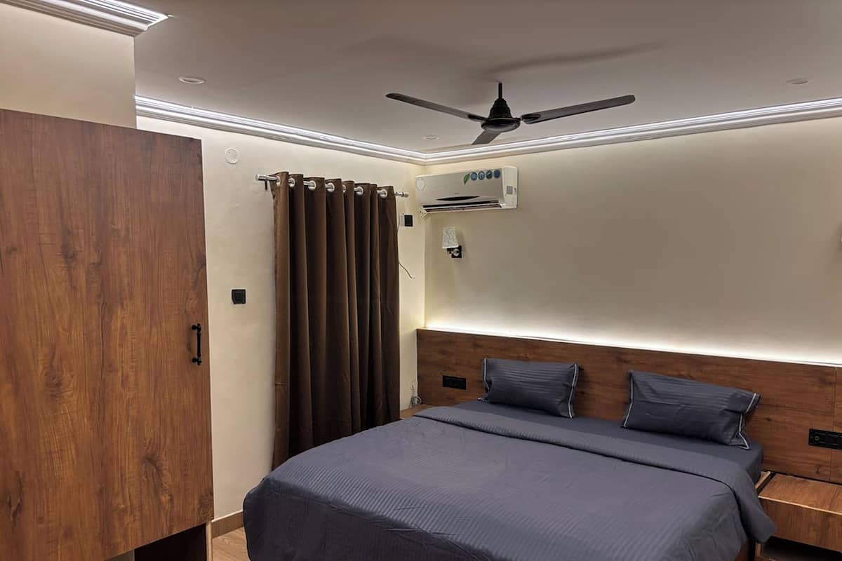 A bedroom with a bed, a ceiling fan, an air conditioning unit, and a wooden wardrobe.