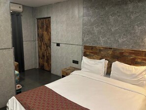 A hotel room with a large bed, a wooden headboard, a grey marble wall, and a wooden door. - Aariv Comforts Baga (Baga)