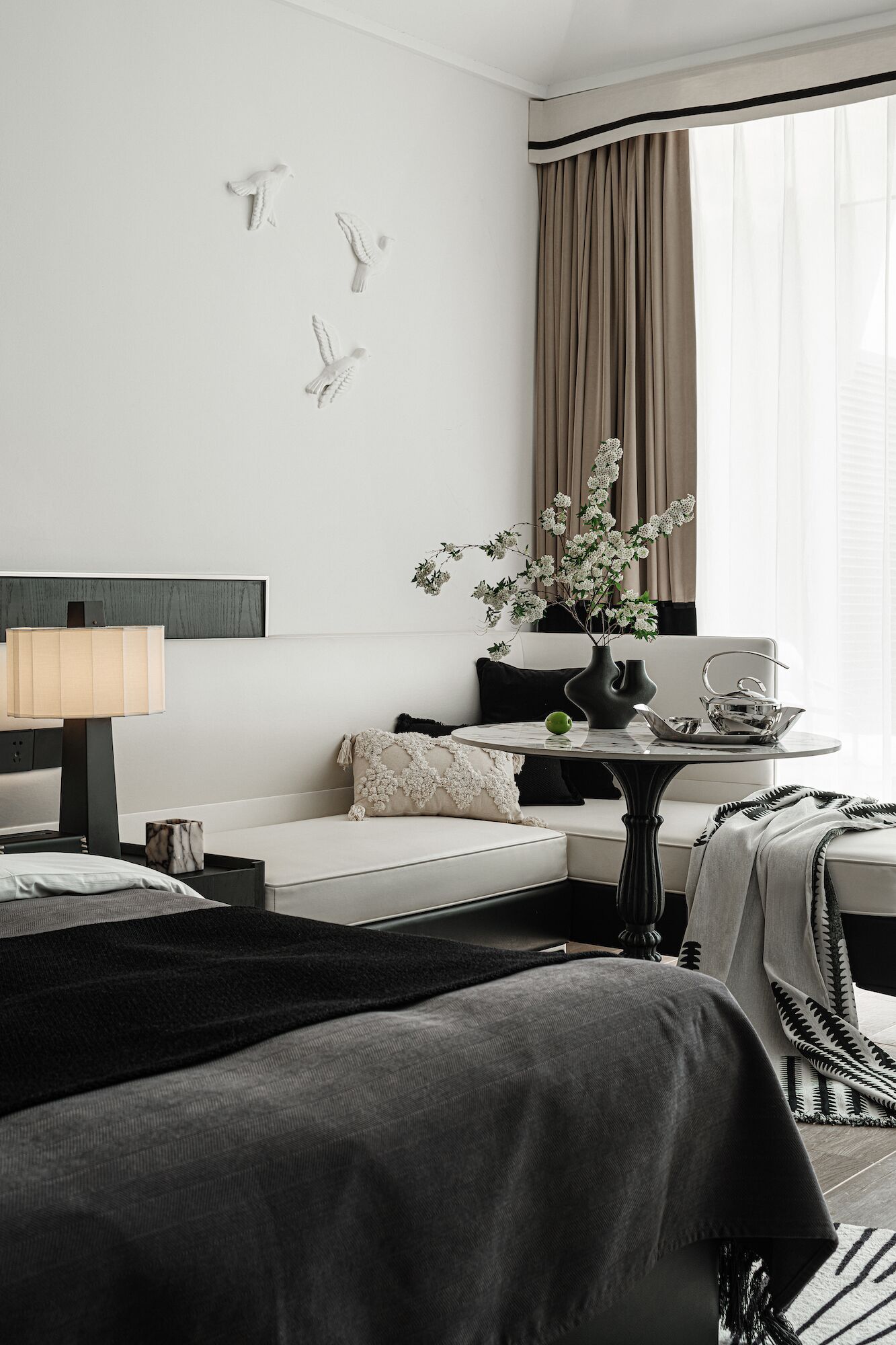 A modern hotel room with a bed, a sofa, a small table, and a window with curtains.