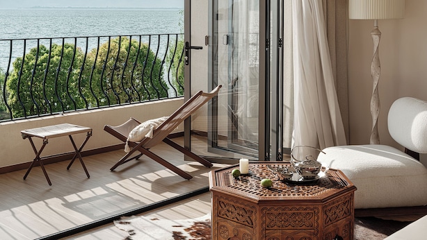 Un balcon avec vue sur la mer, une chaise, une table agrémentée d’objets décoratifs et une lampe.