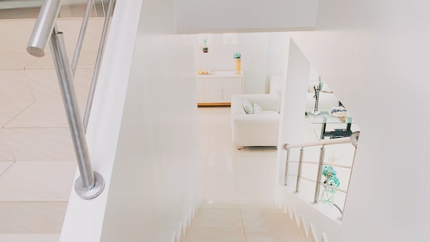 A modern staircase with a metal handrail, leading to a white room with a sofa and a small table with decorative items. - Casa con Piscina Privada para Familias (La Aurora)