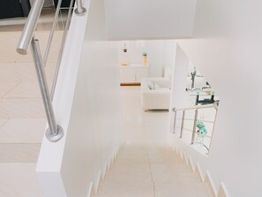A modern staircase with a metal handrail, leading to a white room with a sofa and a small table with decorative items. - Casa con Piscina Privada para Familias (La Aurora)