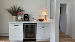 Una cocina moderna con armarios blancos, lavavajillas integrado, cafetera y una pequeña mesa con adornos.
