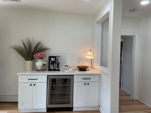 Una cocina moderna con armarios blancos, lavavajillas integrado, cafetera y una pequeña mesa con adornos.