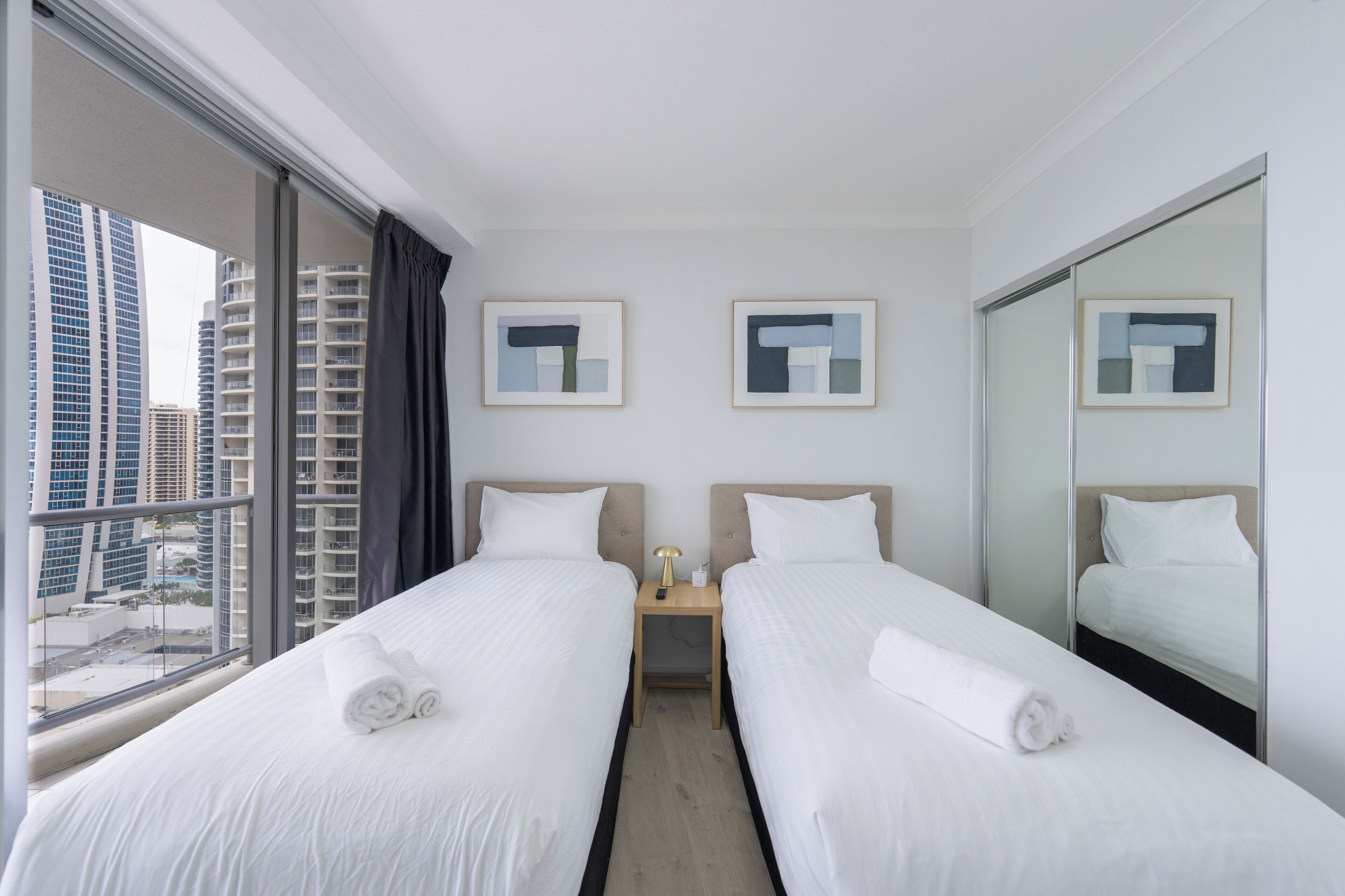 A hotel room with two beds, a nightstand with a lamp, and framed artwork on the walls.