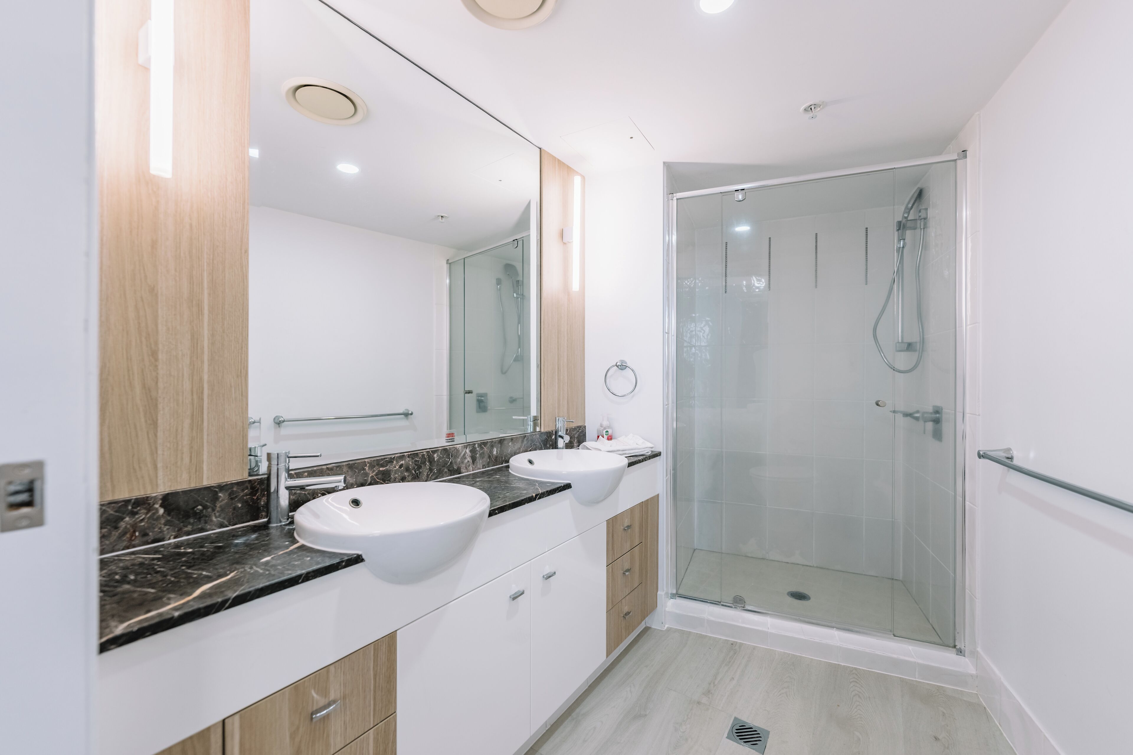 A modern bathroom with two sinks, a glass shower enclosure, and a large mirror.