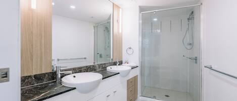 A modern bathroom with two sinks, a glass shower enclosure, and a large mirror.