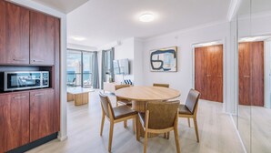 A modern kitchen with wooden cabinets, a dining table with chairs, and a large window offering a city view. - Resort Style Chevron Apartments (Surfers Paradise)