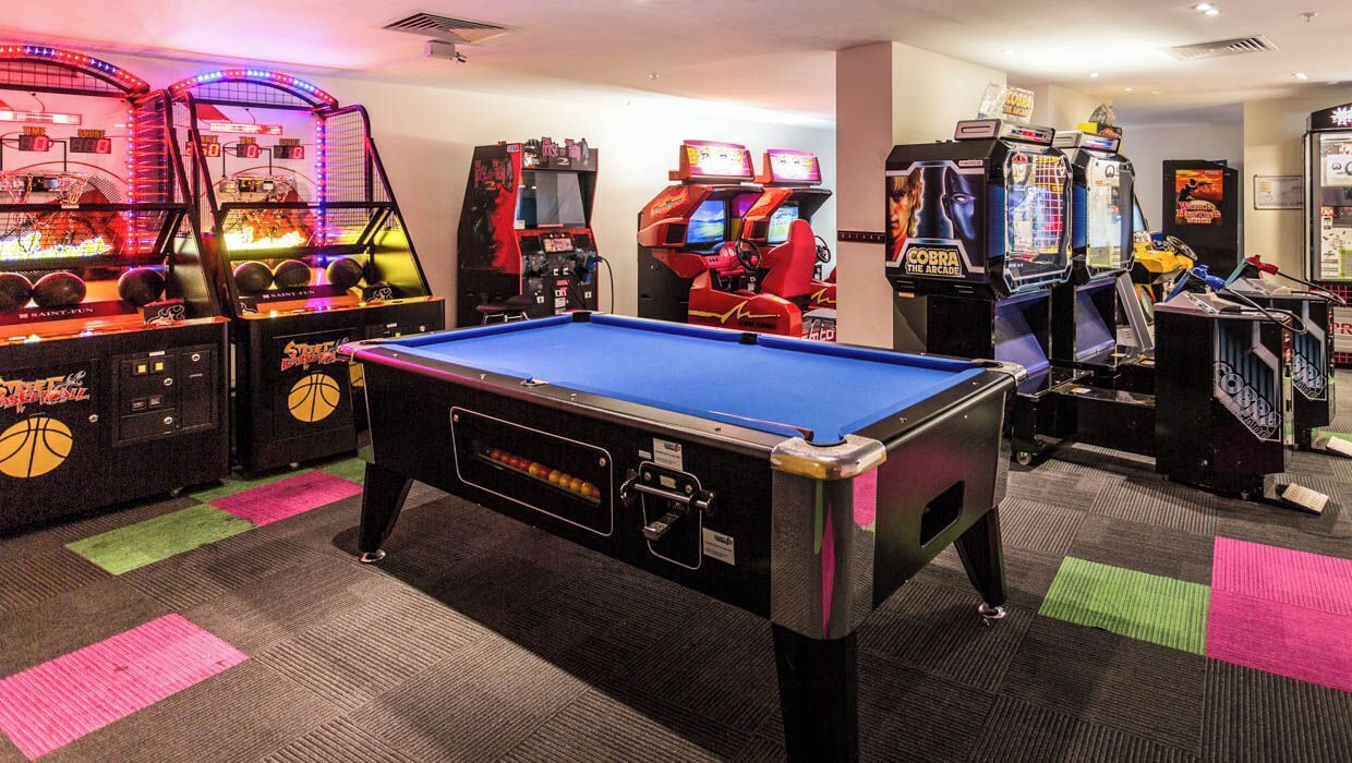 Un tavolo da biliardo circondato da cabinati arcade in una sala con pavimento rivestito di moquette.