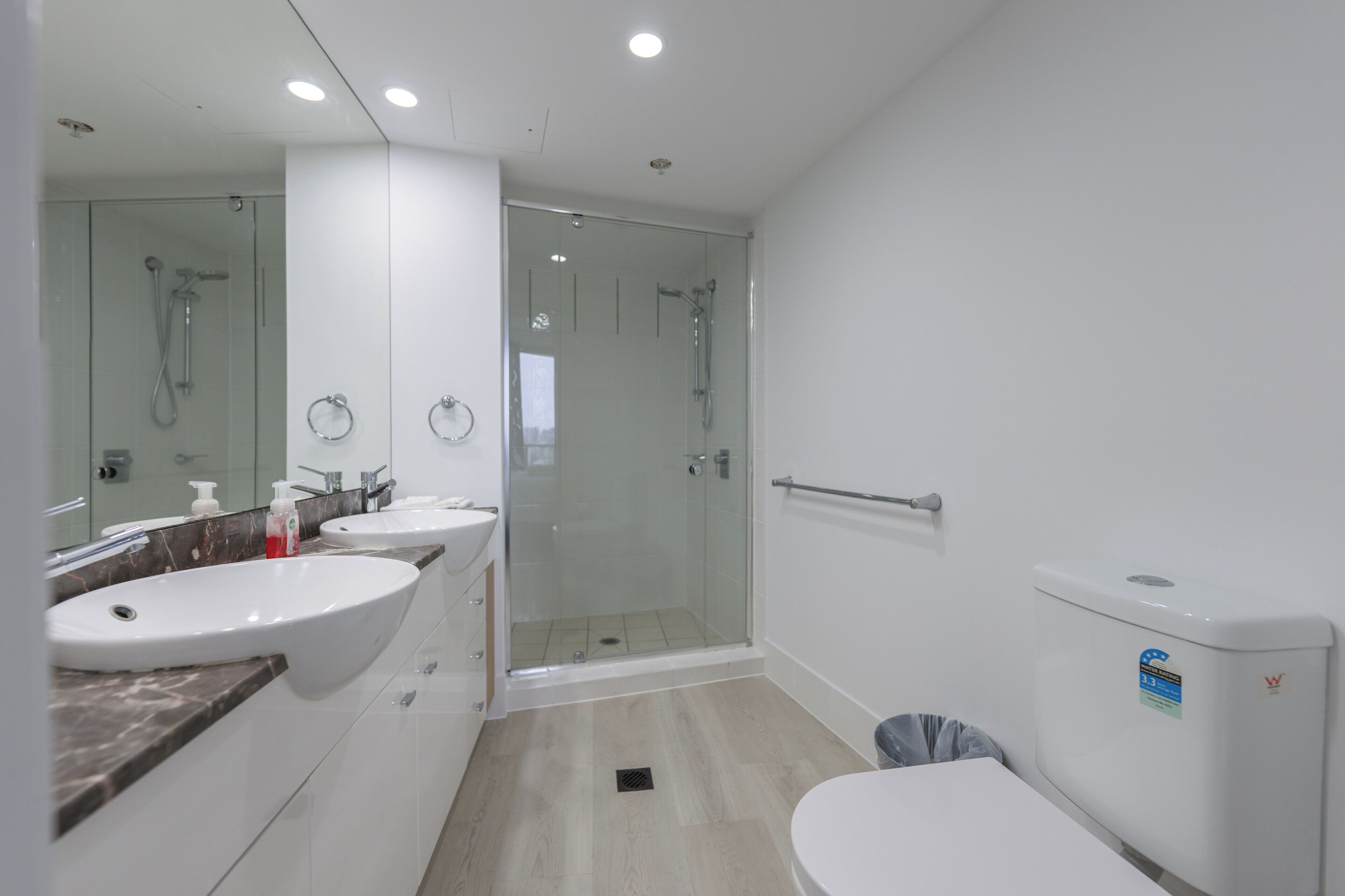 A modern bathroom with a glass-enclosed shower, two sinks, and a toilet.