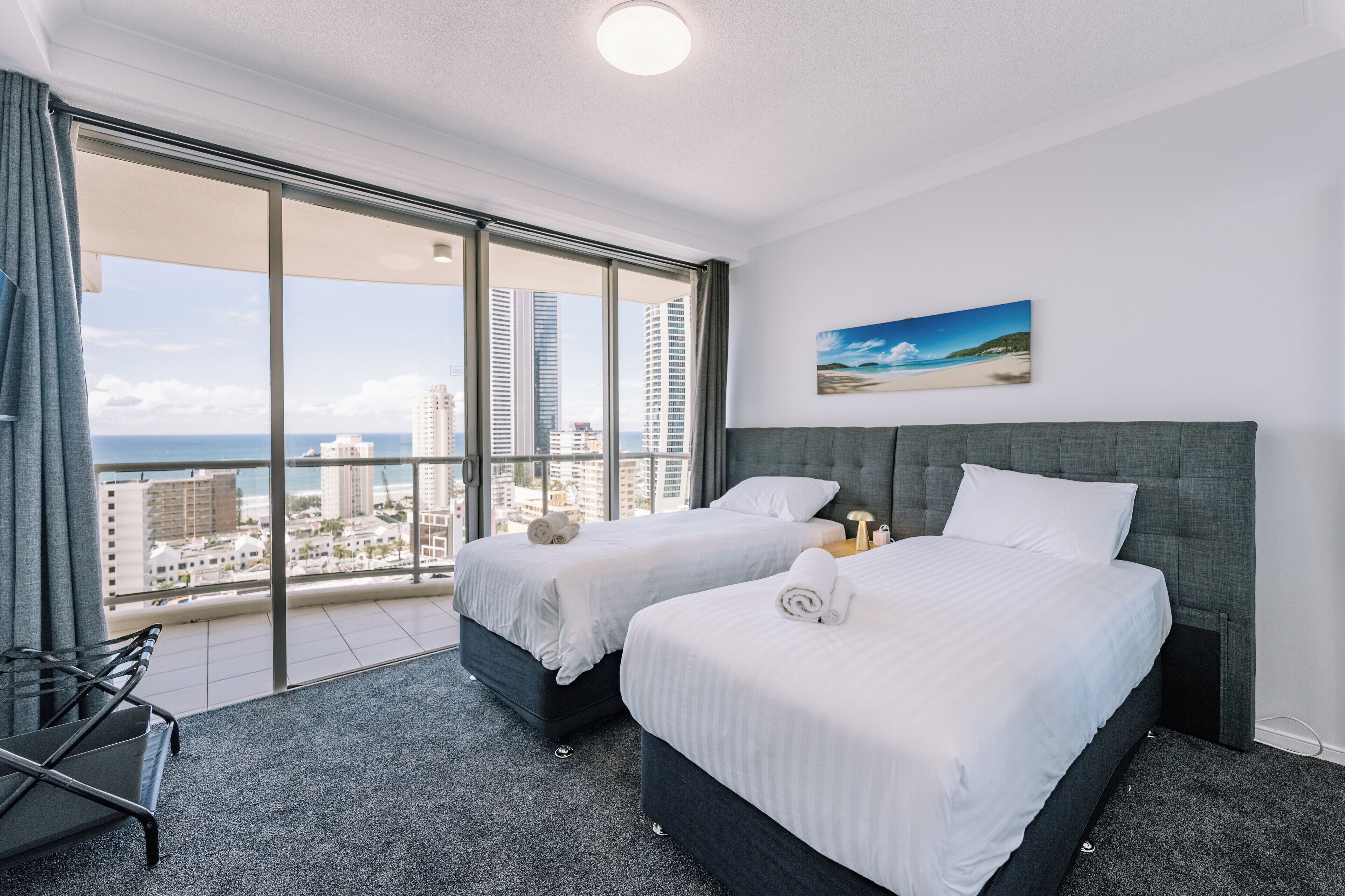 A hotel room with two beds, a large window with a city view, and a painting on the wall.