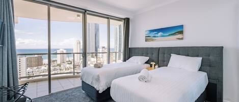 A hotel room with two beds, a large window with a city view, and a painting on the wall.