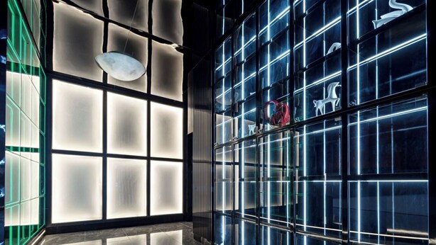 Un intérieur moderne avec un grand mur de verre où sont exposés divers objets et un sol réfléchissant.