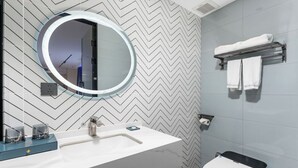 Une salle de bain moderne avec un lavabo blanc, un miroir rond et des toilettes.