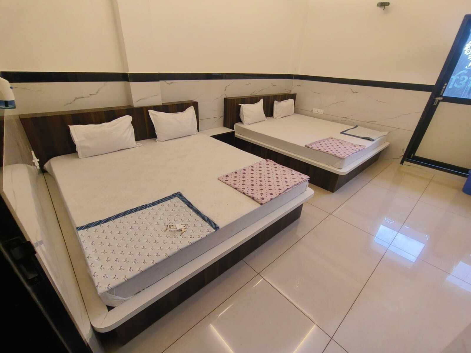 Une chambre d’hôtel avec deux lits, chacun doté d’un matelas blanc et d’une couvre-lit à motifs. La chambre est décorée avec un revêtement mural imitant le marbre et possède un sol carrelé.