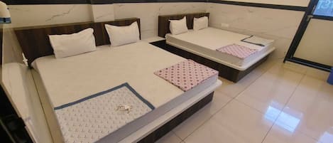 A hotel room with two beds, each with a white mattress and a patterned bedspread. The room has a marble-like wall design and a tiled floor.
