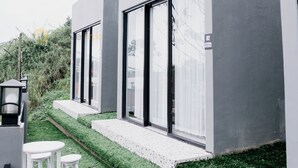 A modern building with large windows and a small outdoor seating area with white stools. - Stigma Kubus By Travelink (Kejajar)