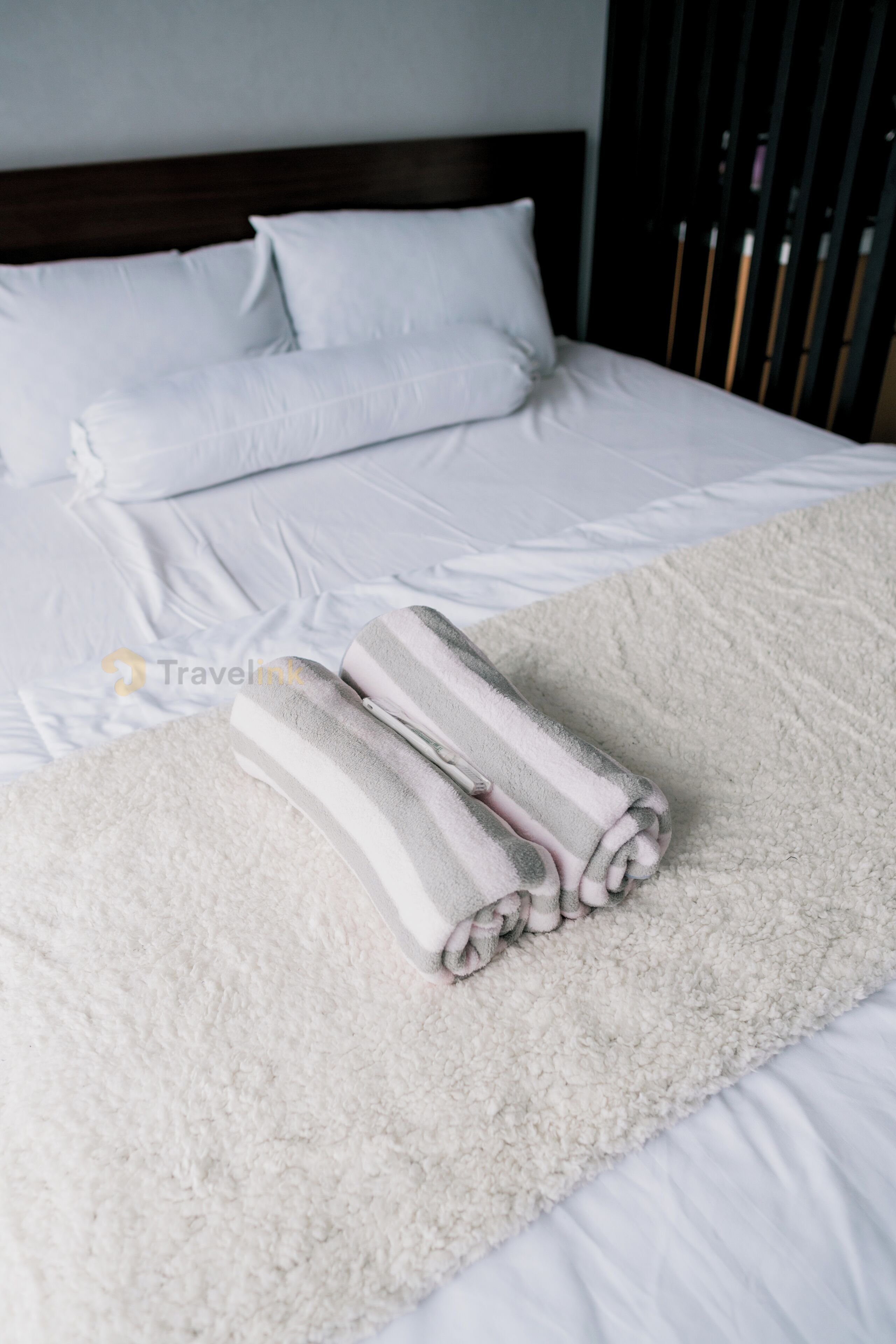 A neatly made bed with white linens and two rolled towels placed on a fluffy white blanket.