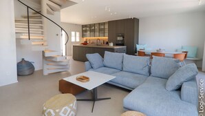 A modern living room with a light blue sectional sofa, a white coffee table, and a staircase with a minimalist design.