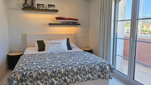A bedroom with a bed, bedside tables, a window, and a shelf with decorative items.