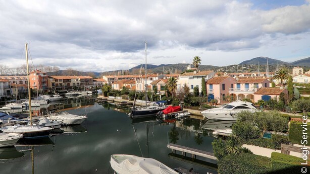 A marina with boats docked, surrounded by residential buildings and a mountainous backdrop.