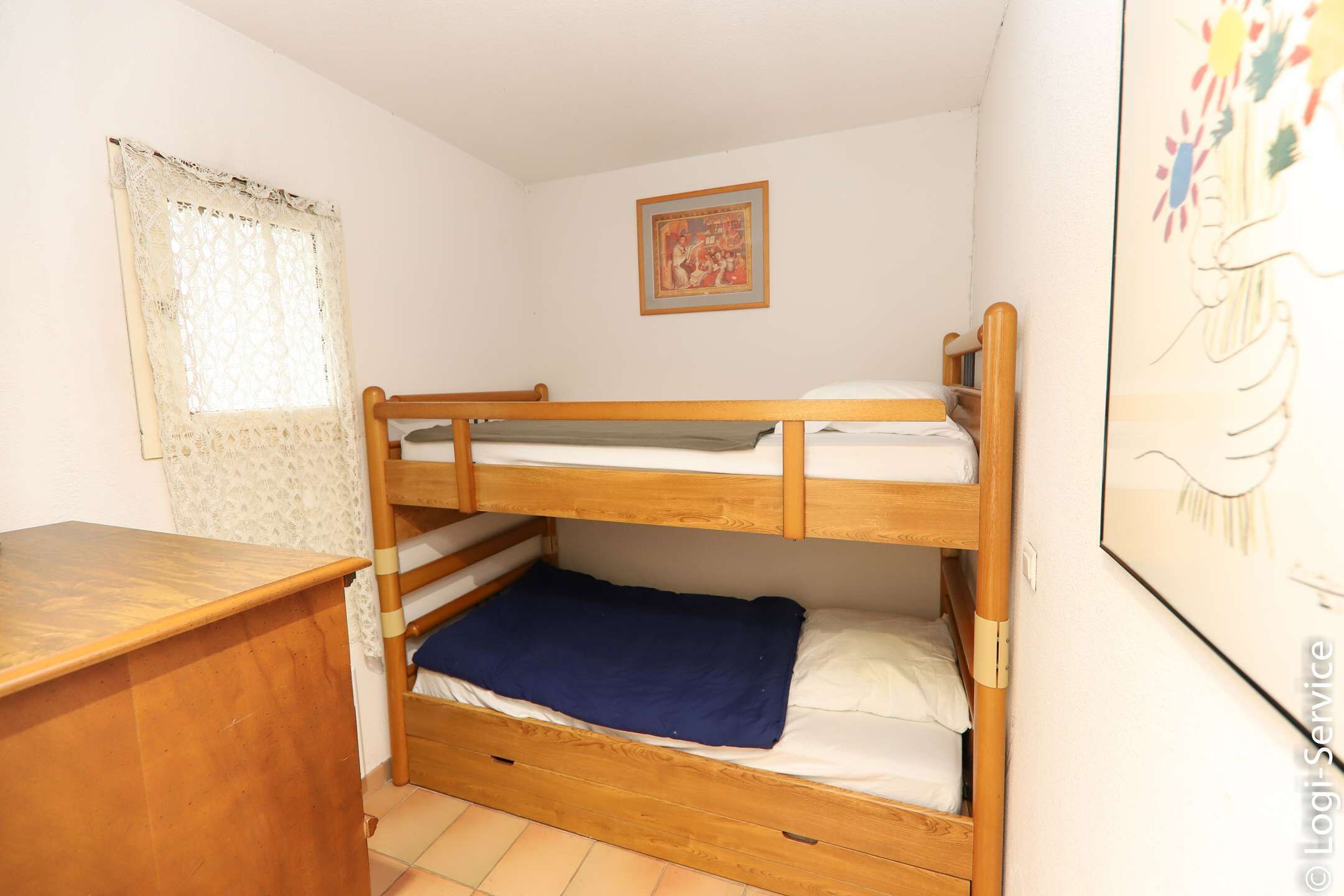Een slaapkamer met een stapelbed, een houten bureau en een kantgordijn.