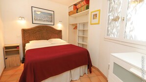 A bedroom with a bed, a ceiling fan, a wardrobe, and a window with patterned curtains.