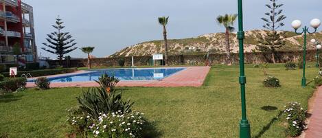 A swimming pool surrounded by well-maintained grass and flowers, with a building in the background.