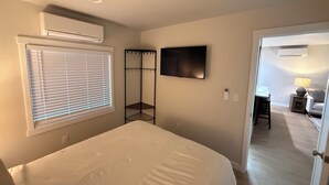 Un dormitorio con cama, televisión, aire acondicionado y ventana con persianas.