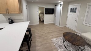Una cucina moderna con mobili in legno, un piano di lavoro bianco e un'area pranzo con sgabelli neri.