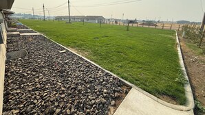Un'area verdeggiante con un sentiero in cemento, pali dell'alta tensione e edifici in lontananza.