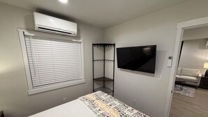 Una camera da letto con un letto, un condizionatore, una TV, un armadio e una porta che dà su un'altra stanza.