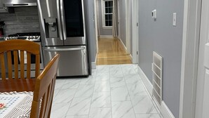 A modern kitchen with stainless steel appliances, a wooden dining table, and a hallway with grey walls and white tiled flooring. - North End Family  (Manchester)