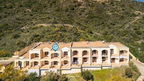 A multi-story building with balconies, set against a hilly backdrop. - Ginestre 13 (Is Molas)