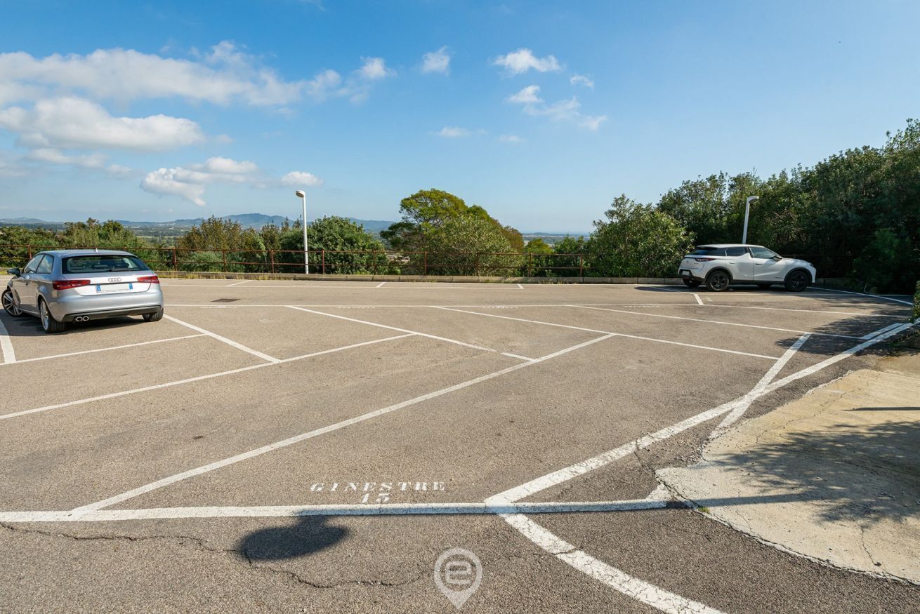 A parking lot with two cars, clear sky, and distant hills.