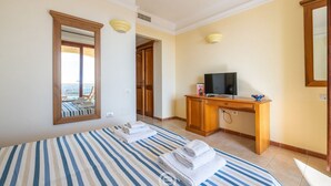 A hotel room with a bed, a desk with a TV, a mirror, and a view of the balcony. - Ginestre 13 (Is Molas)