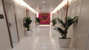 Un pasillo de hotel con suelo de mármol, plantas en macetas y una tela decorativa al final.