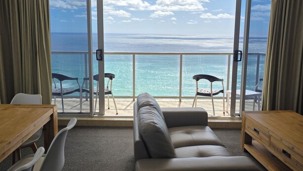 Ein Zimmer mit einer Couch, einem Holztisch und Blick auf das Meer durch große Schiebetüren.