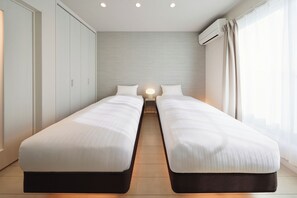 Une chambre d’hôtel moderne équipée de deux lits simples, d’une table de chevet avec une lampe, d’une armoire et d’un appareil de climatisation.