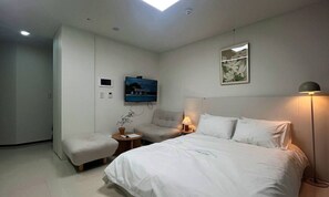 A hotel room with a bed, a chair, a desk, a TV, a lamp, and a painting on the wall. - YEONSAN THE STAY (Busan)