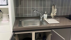 A modern kitchen with a stainless steel sink, a kettle, and a coffee maker. There are cabinets above the sink and a countertop with a dish rack. - YEONSAN THE STAY (Busan)