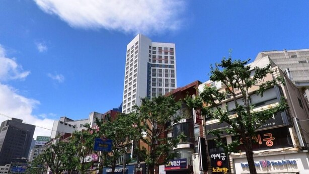 A tall building with a modern design, surrounded by various commercial buildings and trees. - YEONSAN THE STAY (Busan)